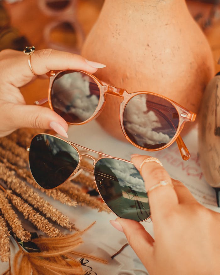 Close-up of hands holding stylish sunglasses reflecting autumn scenery.