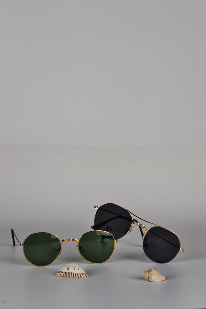 Two pairs of sunglasses and seashells on a minimal gray surface. Perfect for summer fashion concepts.