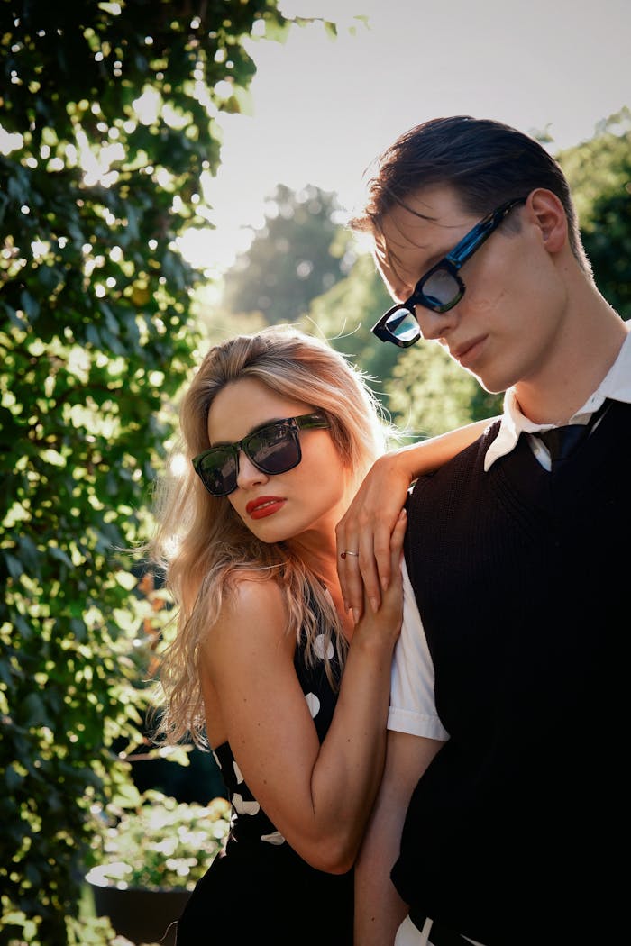 A fashionable couple poses with sunglasses in a sunny outdoor setting, exuding modern style.